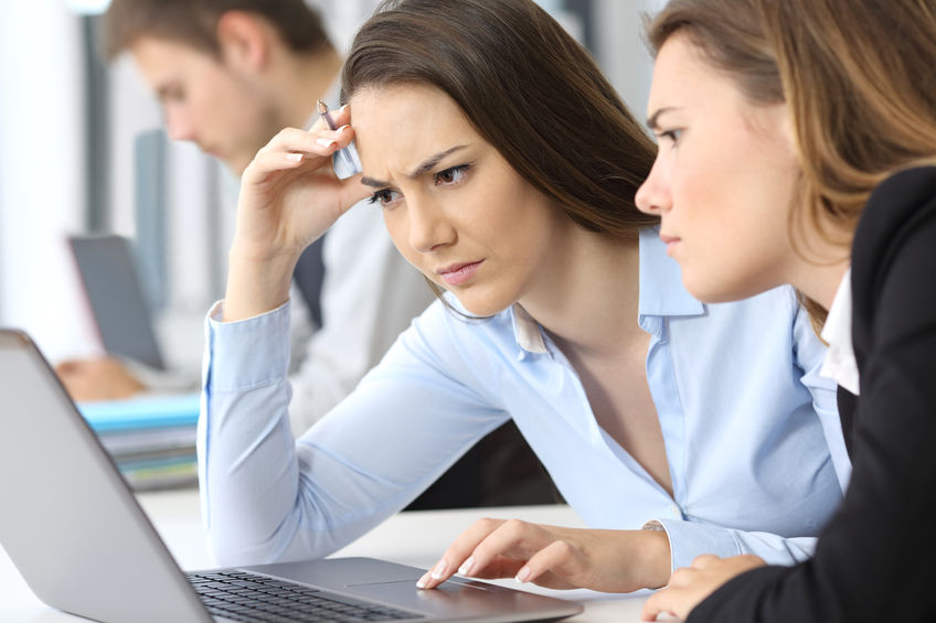 Two confused businesswomen working online with a laptop at office